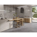 Modern kitchen interior with a light wood island table and three matching bar stools, set against gray stone-look tile walls and floor. A black range hood, pendant lights, and large glass doors showing an outdoor patio are visible.